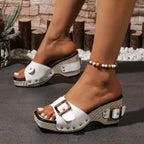 White clogs with brown buckles worn by a person, with a rustic background.