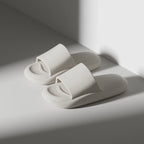 Pair of white slippers on a light gray surface with soft shadows.