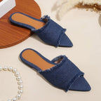 Blue denim slippers on a light beige surface with a pearl necklace.
