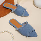 Pair of blue denim slippers on a beige surface with a pearl necklace.