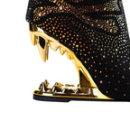 Black high-heeled shoe with gold stiletto heel and rhinestone embellishments on a white background