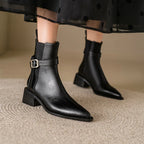 Black leather ankle boots with a buckle on a neutral background