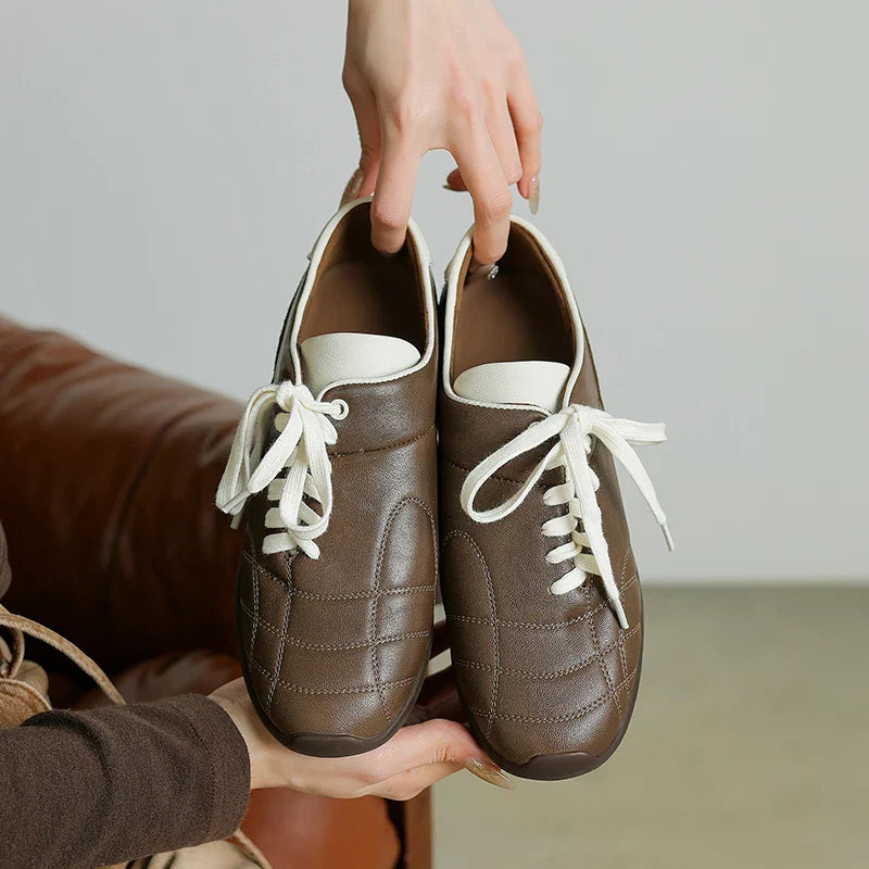 Brown leather shoes with white laces held by a person against a neutral background