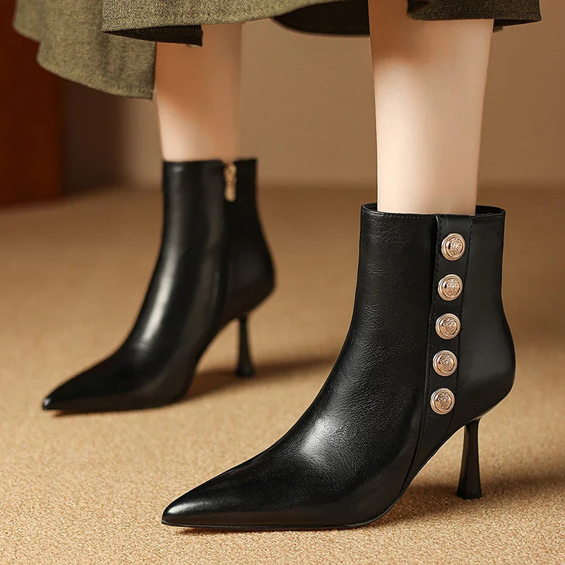Black high-heeled ankle boots with decorative buttons on a beige background