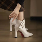 White high-heeled boots with a red sole worn by a person, on a blurred background.