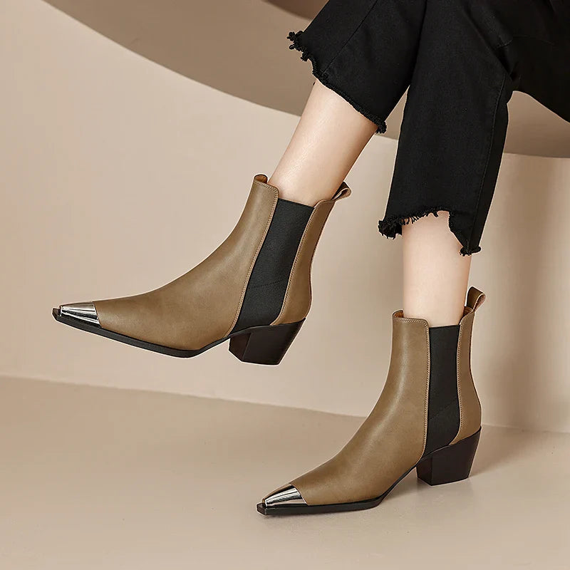 Brown ankle boots with metallic toe tips worn by a person on a beige background