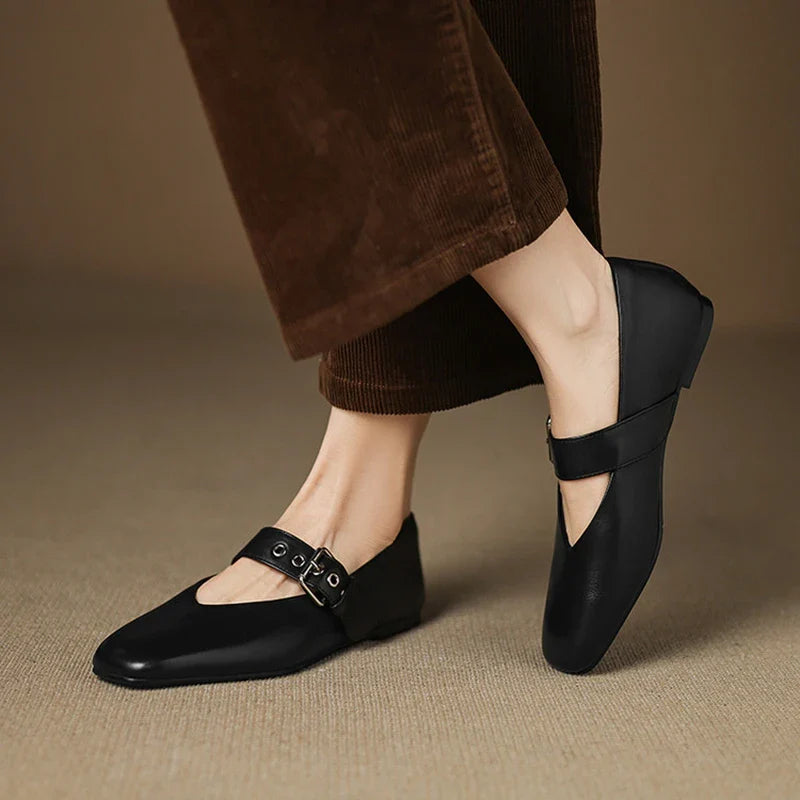 Black shoes with buckles worn by a person on a beige background